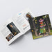 An open printed Pefect Bound Brochure displayed on a light grey studio background. The cover shows a colorful painted figure in a hat and coat with the text 'Pyele Art Museum Annual 2025' and '100th Anniversary.